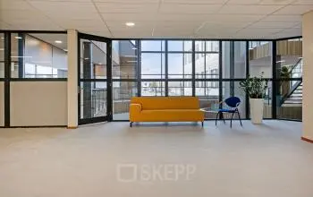 Grote open ruimte in het kantoorpand op De Run 4312, Veldhoven met glazen wanden, geel bankstel en interieurplanten. Ideaal voor kantoorruimte huren.