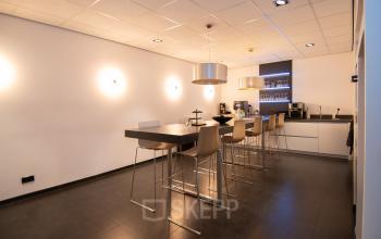 Moderne kantoorpand op Gildestraat 13 in Velp met een strakke pantry voorzien van hoge tafels, stijlvolle barkrukken en professionele koffieapparatuur. Ideaal om te huren voor ontspanning en informele bijeenkomsten.