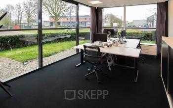 Kantoorruimte te huur op Gildestraat 13 in Velp, met uitzicht naar buiten door grote ramen. Twee bureaus met stoelen en computers, modern en functioneel ingericht.