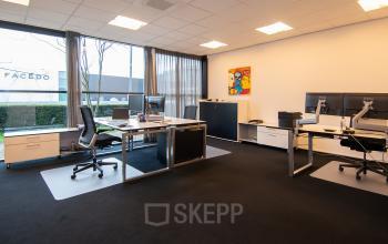 Heldere kantooruimte te huur op Gildestraat 13 in Velp met moderne inrichting en grote ramen voor veel natuurlijk licht. Twee bureaublokken uitgerust met computerschermen en comfortabele stoelen.