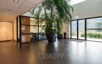 Ruime entree van het kantoorpand op Gildestraat 13 in Velp, met grote groene planten en zicht op vergaderruimte. Ideaal om kantoorruimte te huren.
