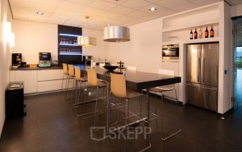 Moderne gemeubileerde pantry op Gildestraat 13 in Velp, ideaal voor kantoorruimte huren met hoge stoelen aan de bar en apparatuur zoals een koffiezetapparaat en koelkast.