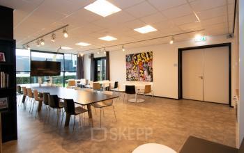 Ruime kantoorruimte in Velp met moderne tafels en stoelen, ideaal voor vergaderingen of presentaties. Opvallend kunstwerk aan de muur in een lichte, uitnodigende sfeer.