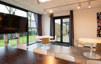 Moderne kantoorruimte huren aan de Gildestraat 13 in Velp, voorzien van ruime tafels en stoelen met veel natuurlijk lichtinval en toegang tot een kleine buitenruimte.
