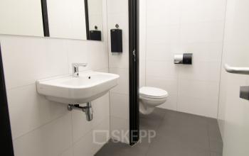 Modern toilet binnen kantoorpand aan de Gildestraat 13, Velp. Strakke witte tegels met grijze vloer ondersteunen een functionele uitstraling. Ideaal voor degenen die kantoorruimte huren voor een efficient en professioneel gebruik.