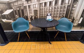 Kantoorruimte huren in Venlo met een kleine ronde tafel en twee moderne stoelen tegen een muur met vintage afbeelding.