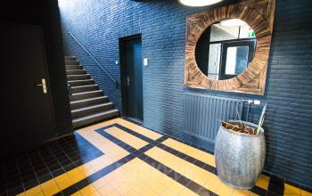 Entree van een kantoorpand aan de Kaldenkerkerweg 28 in Venlo. Een moderne ruimte met grote spiegel, tegels in geel-zwart patroon en een trap naar boven. Kantoorruimte huren mogelijk.