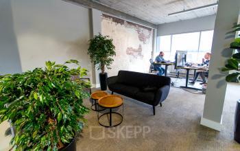 Kantoorruimte in Venlo op Kaldenkerkerweg 20 met moderne inrichting, groene planten en een zithoek. Twee personen werken aan bureaus bij het raam.