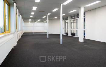 Kantoorruimte huren op Parlevinkerweg 1 in Venlo. Grote, lichte ruimte met grijze vloerbedekking, glazen wanden en meerdere ramen.