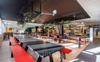 Gemeubileerde kantoorruimte in Lange Dreef 10, Vianen Utr, met lange tafels en rode banken, geschikt voor werk en informele bijeenkomsten. Veel natuurlijk licht en groene planten aanwezig.