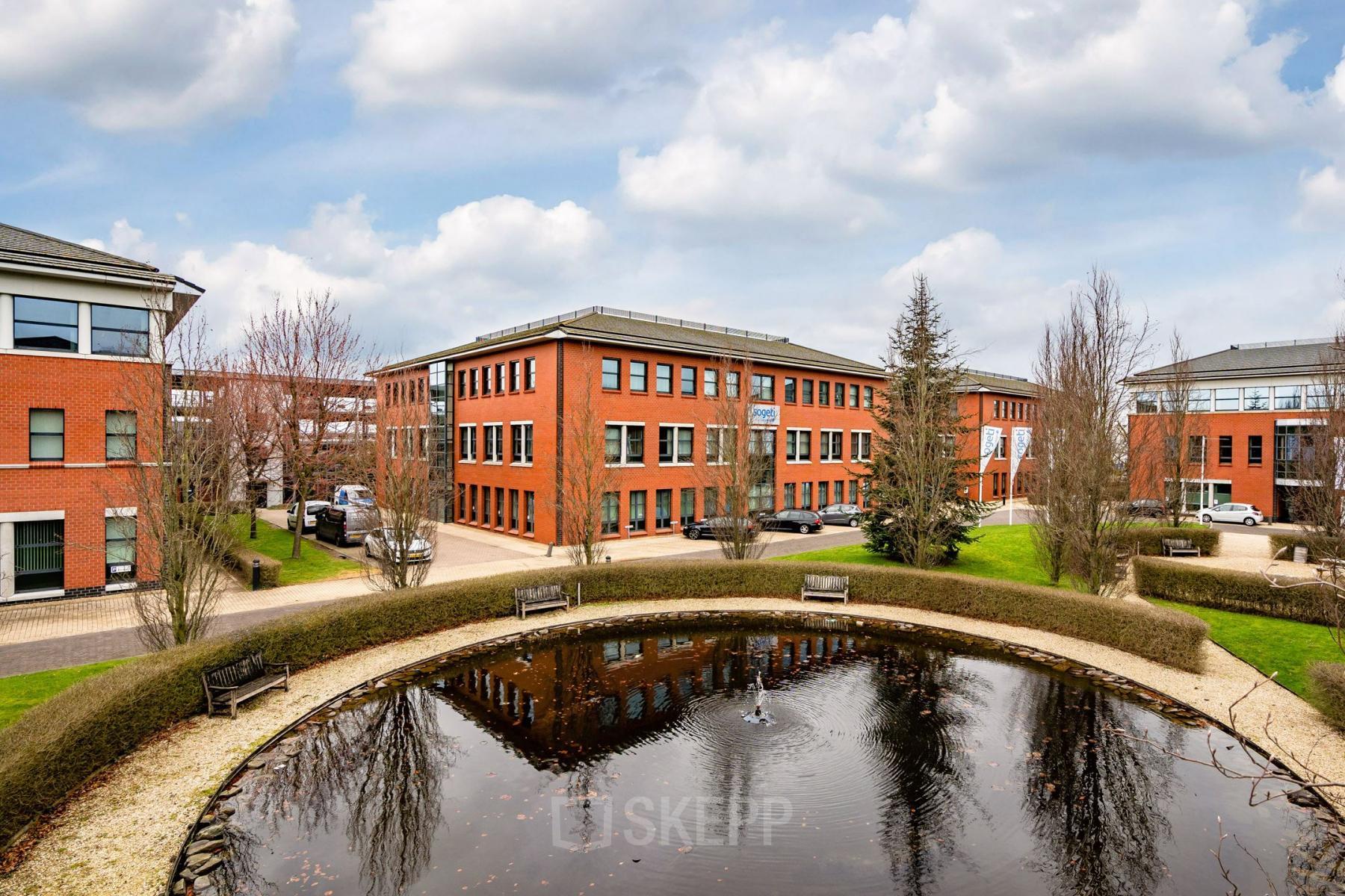 Exterieur van het kantoorpand op Lange Dreef 10, Vianen Utr. Rode bakstenen gebouw omgeven door groen met een vijver op de voorgrond. Geschikt voor kantoorruimte huren.