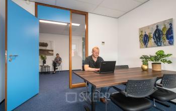 Kantoorpand aan Witboom 1, Vianen Utr, met twee mensen bezig met laptops in een ingerichte werkruimte. Houten tafel omringd door stoelen en moderne kunst aan de muur.