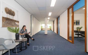 Lichte kantoorruimte op Witboom 1, Vianen Utr met een wachtende vrouw die in een tijdschrift leest. De ruimte heeft blauwe vloerbedekking en kunst aan de muur.