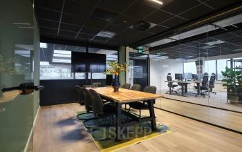 Modern ingerichte kantoorruimte met glazen wanden en houten tafel, gelegen op Havenweg 24 in Vianen Utr, ideaal om een kantoor te huren. Verschillende bureaus zijn zichtbaar door de glazen wanden.