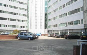 Parkeerplaats bij kantoorpand op Regulusweg 11 in Voorburg, met meerdere geparkeerde auto's en moderne gevels van het gebouw. Ideale locatie voor kantoorruimte huren.