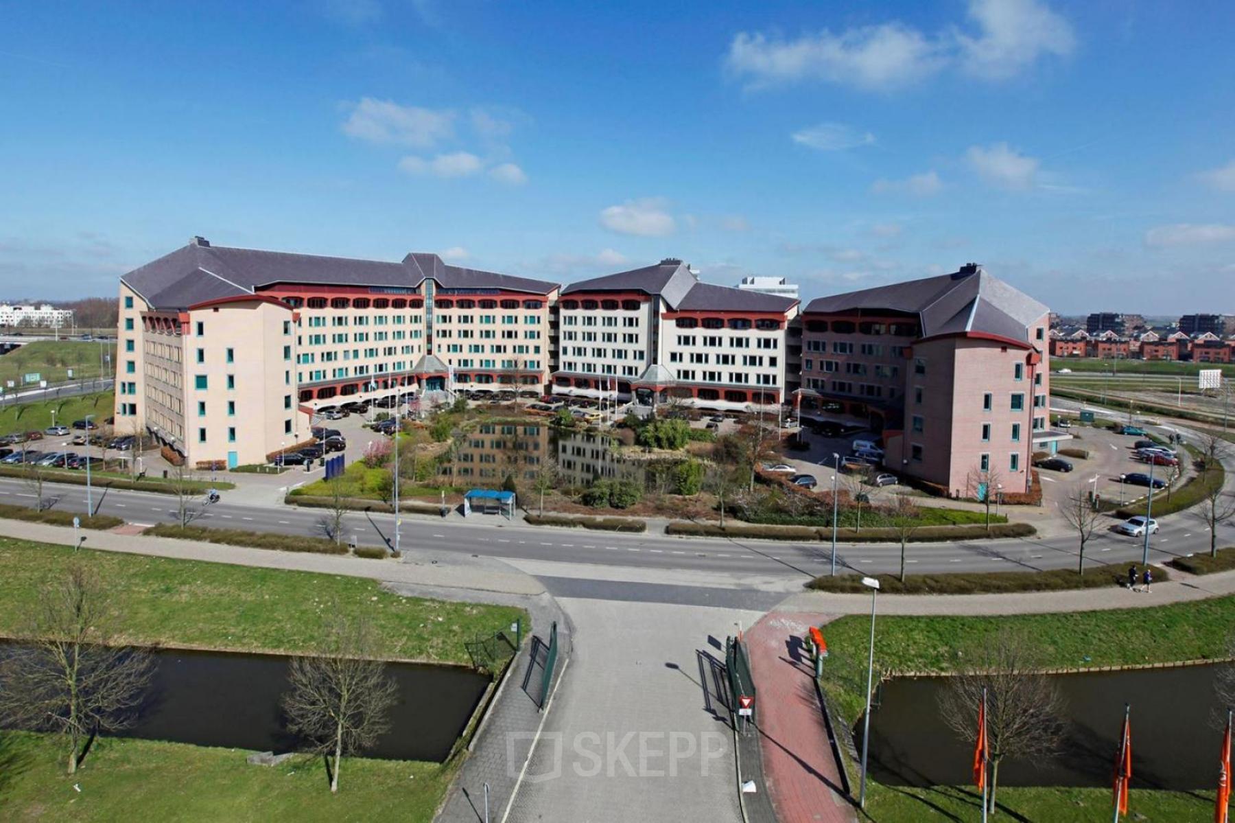 Buitenaanzicht van een groot kantoorpand gelegen aan Loire 104 - 206 in Voorburg met parkeerplaats ervoor.