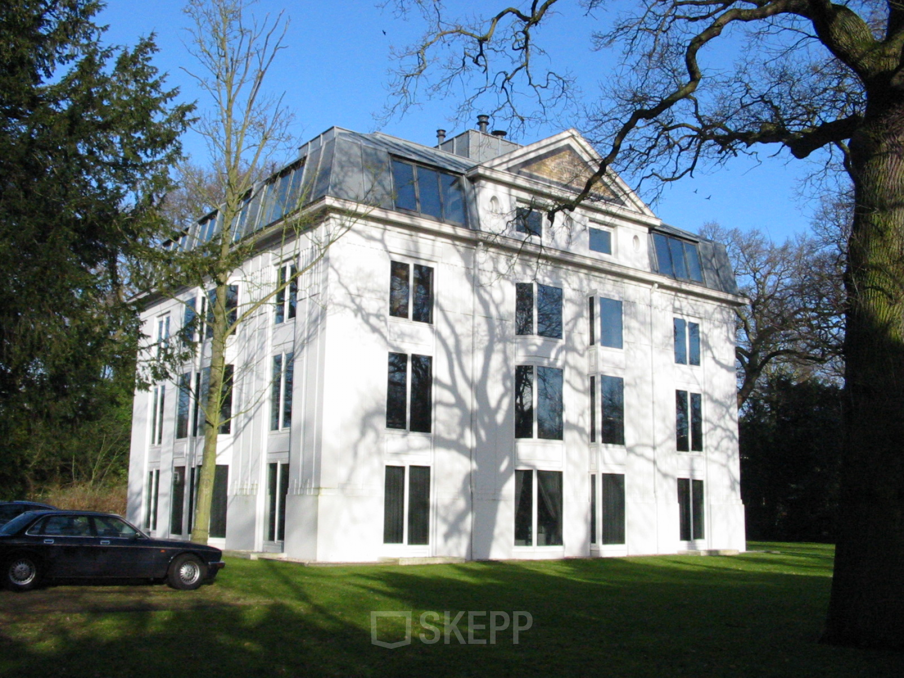 Exterieur van het kantoorpand aan Van der Oudermeulenlaan 1, Wassenaar. Modern wit gebouw met grote ramen en omliggende groene tuin.