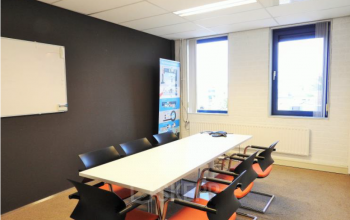 Moderne vergaderruimte binnen kantoorpand aan Pompmolenlaan 9 in Woerden met oranje stoelen en witte tafel.