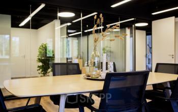 Moderne vergaderruimte in kantoorpand op Pelmolenlaan 16, Woerden, met glazen wanden, comfortabele stoelen en decoratieve elementen op een houten tafel.
