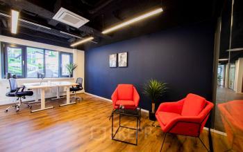 Kantoren huren op Pelmolenlaan 16 in Woerden met moderne inrichting; twee rode stoelen en een bureau met stoelen, houten vloer en donkere muur, geschikt voor werk.