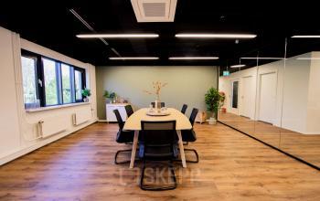 Moderne vergaderruimte in kantoorpand op Pelmolenlaan 16, Woerden, met houten vloer, spiegelwand en grote tafel met stoelen. Geïntegreerde verlichting en planten voor een frisse sfeer.
