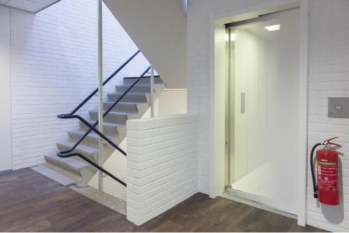 Ingang van een kantoorpand op Pompmolenlaan 9, Woerden, met een open lift en trap. Ideaal voor wie kantoorruimte wil huren. Heldere verlichting en praktische indeling creëren een professionele uitstraling.