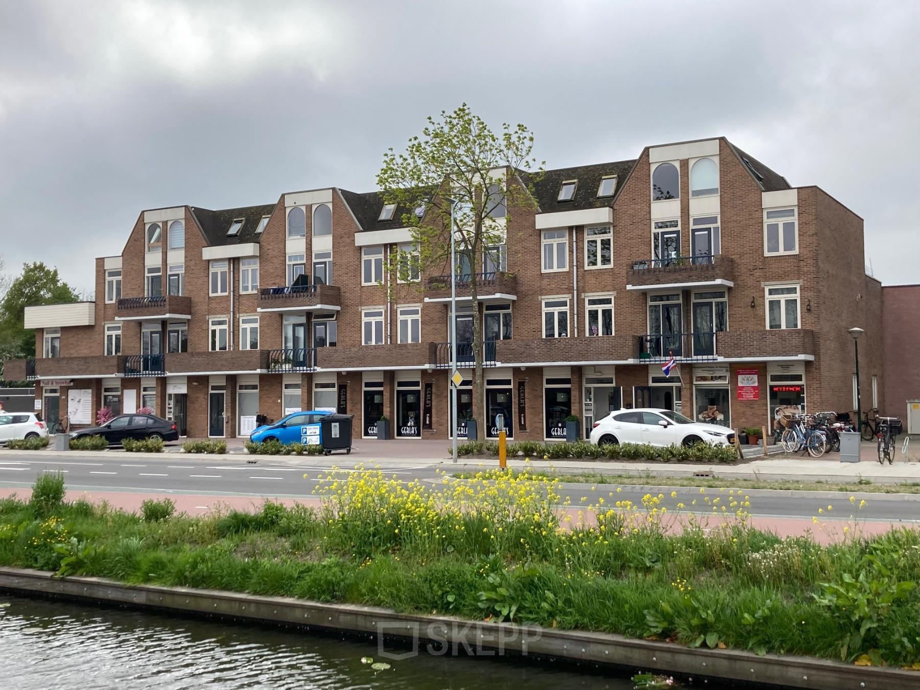 Buitenaanzicht van het kantoorpand aan Boerendijk 8 in Woerden met meerdere winkels op de begane grond en parkeermogelijkheden aan de voorzijde.