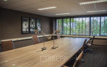 Kantoorruimte huren in Woerden, Zaagmolenlaan 4-1: vergaderruimte met grote houten tafel, lederen stoelen en bureauverlichting met zicht op groen buiten.