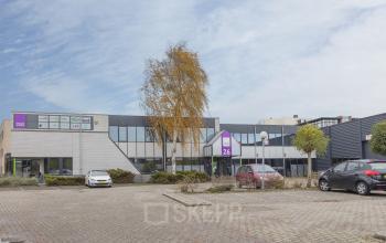 Exterieur van kantoorpand Pompmolenlaan 26 in Woerden, met parkeerplaatsen en auto's op de voorgrond.