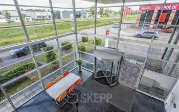 Moderne entree met hoge glazen ramen en een ronde draaideur in kantoorpand Oude Blaauwweg 5, Wormerveer, geschikt voor mensen die kantoorruimte willen huren.