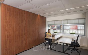 Moderne kantoorruimte huren aan de Oude Blaauwweg 5 in Wormerveer met een persoon bezig met laptopwerk aan een tafel voor een groot raam.