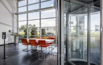 Ingang van kantoorpand aan Oude Blaauwweg 5, Wormerveer. Moderne glazen deuren met uitzicht op groene omgeving. Ideaal voor kantoorruimte huren met uitnodigende entree voor bezoekers.