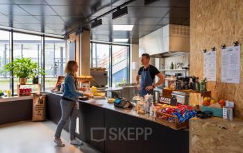 Moderne pantry in een kantoorpand aan de Boerhaavelaan 40, Zoetermeer, met een medewerker achter een balie en een vrouw die koffie haalt.