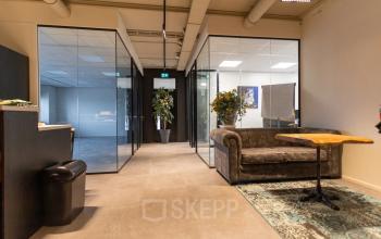 Moderne kantoorruimte in Zoetermeer met glazen wanden, een grijze bank en een houten tafel, geschikt voor vergaderingen of informeel overleg. Kantoorruimte huren op Boerhaavelaan 40.
