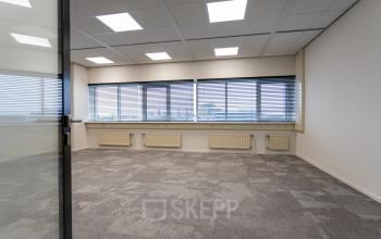 Kantoorruimte te huur in het kantoorpand op Boerhaavelaan 40, Zoetermeer. De ruimte heeft grote ramen met jaloezieën en grijze vloerbedekking.