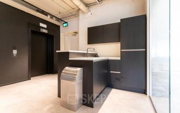 Moderne pantry in kantoorpand aan de Boerhaavelaan 40, Zoetermeer, geschikt voor kantoorruimte huren. Strakke, donkere kasten met een gootsteen en subtiele verlichting. Perfect voor dagelijks gebruik door kantoorpersoneel.