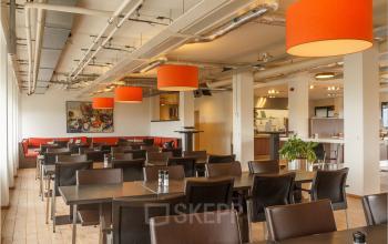 Ruime kantoorpand-interieur aan Bredewater 26, Zoetermeer, met moderne zitplaatsen en opvallende oranje lampen. Ideaal voor bedrijven die kantoorruimte willen huren met gemeubileerde werkplekken. Een uitnodigende plek voor zakelijke ontmoetingen.