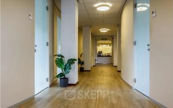 Hal met houten vloer en glazen deuren, accentueert toegang tot diverse kantoorruimtes in kantoorpand Bredewater 26 in Zoetermeer. Planten in potten verlevendigen de rustige sfeer.