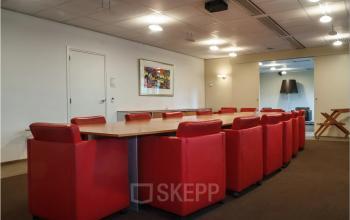 Ruime vergaderruimte in Zoetermeer met rood meubilair en grote houten tafel, ideaal voor kantoorruimte huren op Bredewater 26.