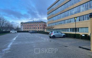 Kantoorpand aan de Baron de Coubertinlaan 35 in Zoetermeer, met parkeerplaatsen en blauwe lucht. Ideale locatie voor kantoorruimte huren.