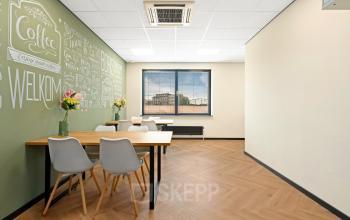 Moderne kantoorpand ingericht als ontmoetingsruimte met houten vloer, groene wanddecoratie en tafel met stoelen. Voor een flexibele kantoorruimte huren in Zwijndrecht, Stationsplein 4.