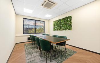 Een lichte vergaderruimte in een kantoorpand op Stationsplein 4, Zwijndrecht, met groene stoelen en een natuurlijke wanddecoratie. Ideale kantoorruimte huren voor professionele bijeenkomsten.