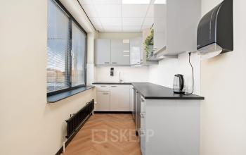 Moderne pantry in kantoorpand op Stationsplein 4, Zwijndrecht, voorzien van strakke keukenkasten, een waterkoker en een groot raam. Perfecte locatie om kantoorruimte te huren. Functioneel en uitnodigend ontwerp.