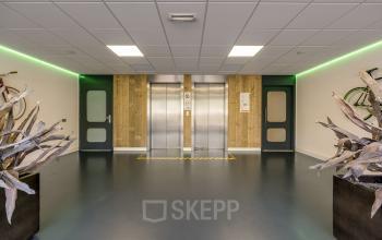 Binnenkant van het kantoorpand op Stationsplein 4 in Zwijndrecht, met een moderne lift en groene verlichting, ideaal voor wie kantoorruimte wil huren.