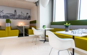 Lichte en moderne kantoorruimte in kantoorpand in Zwolle, Grote Voort 293, met zitbanken en tafels bij grote ramen. De ruimte is geschikt voor informele vergaderingen of als lunchplek.