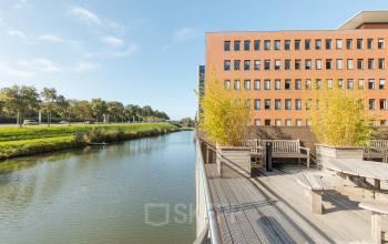 Exterieur van kantoorpand aan de Zuiderzeelaan 27-41 in Zwolle, met uitzicht op een kanaal en buitenzitje. Ideaal voor kantoorruimte huren in een rustige omgeving.