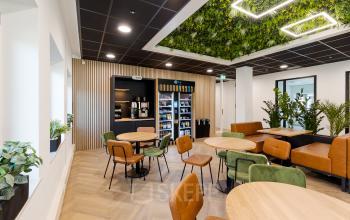 Moderne en uitnodigende kantineruimte met groene accenten aan de Zuiderzeelaan 27-41 in Zwolle. Ideaal voor ontspanning tijdens het kantoorwerk. Stoelen en tafels zijn stijlvol gemeubileerd, met planten voor een frisse sfeer.