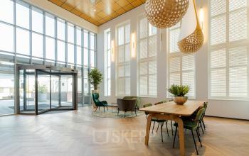 Een lichte en ruime ingang van het kantoorpand op Zuiderzeelaan 27-41 in Zwolle, met moderne meubels en grote ramen. Ideaal voor wie kantoorruimte huren overweegt.