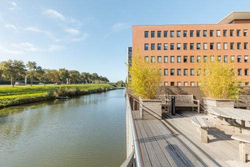 Exterieur van kantoorpand aan de Zuiderzeelaan 27-41 in Zwolle, met uitzicht op een kanaal en buitenzitje. Ideaal voor kantoorruimte huren in een rustige omgeving.