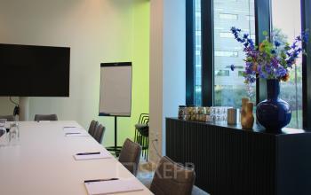 Kantoorruimte huren in Zwolle aan Zwartewaterallee 56. Het kantoorpand heeft een vergaderruimte met grote tafel, stoelen, flipchart en decoratieve bloemenvaas.